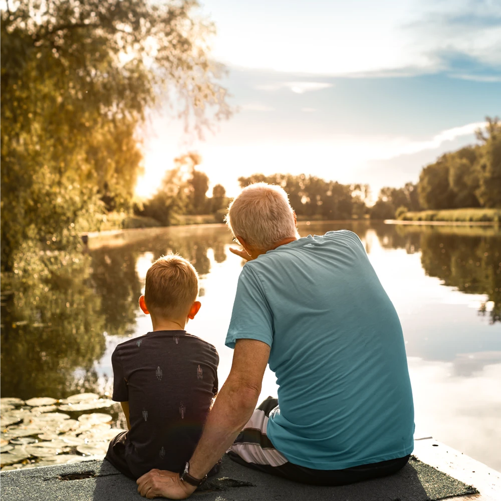 grandfather and son sitting next to a lake